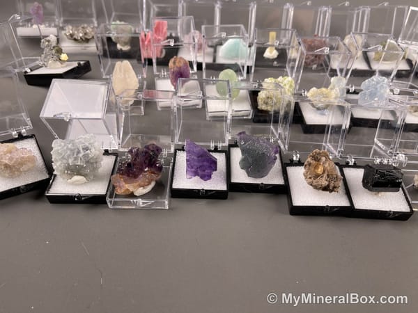 Bulk004 actual mixed mineral specimen box with about 35 different mini natural specimens, including likely fluorite, black tourmaline, quartz, stibnite, grape agate and green prehnite-type material.