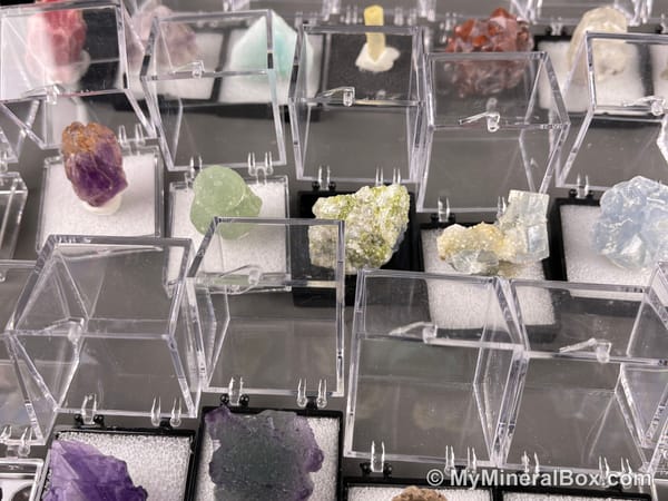 Bulk004 actual mixed mineral specimen box with about 35 different mini natural specimens, including likely fluorite, black tourmaline, quartz, stibnite, grape agate and green prehnite-type material.
