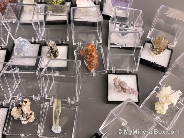 Bulk004 actual mixed mineral specimen box with about 35 different mini natural specimens, including likely fluorite, black tourmaline, quartz, stibnite, grape agate and green prehnite-type material.