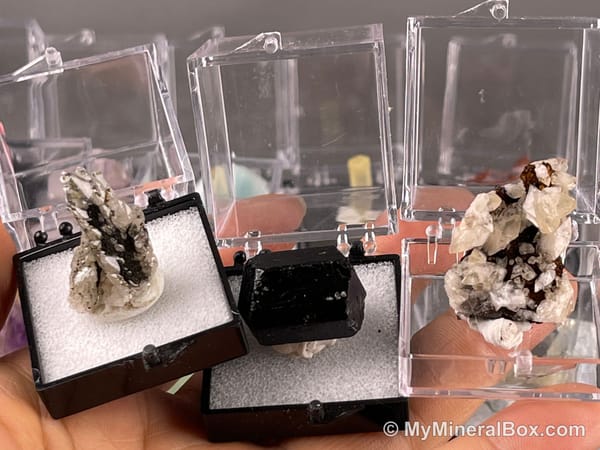 Bulk004 actual mixed mineral specimen box with about 35 different mini natural specimens, including likely fluorite, black tourmaline, quartz, stibnite, grape agate and green prehnite-type material.