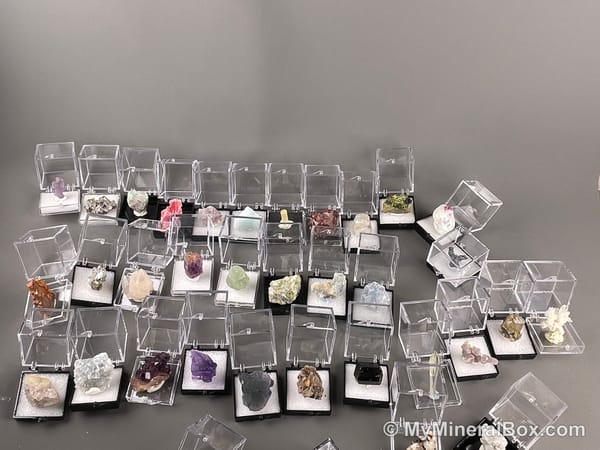 Bulk004 actual mixed mineral specimen box with about 35 different mini natural specimens, including likely fluorite, black tourmaline, quartz, stibnite, grape agate and green prehnite-type material.