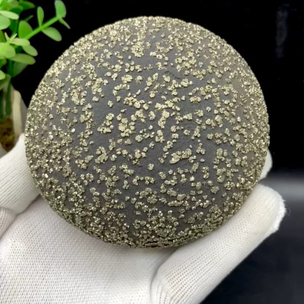 Iron concretion sphere dusted with pyrite from Yunnan, China, held in gloved hand