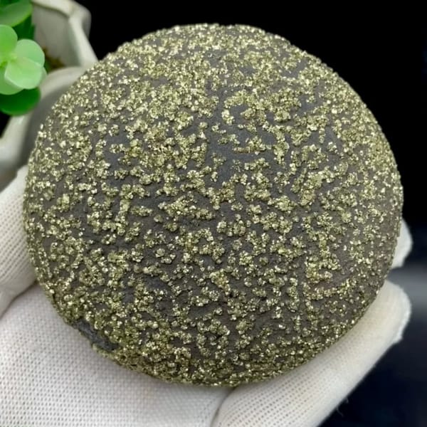 Iron concretion sphere speckled with pyrite from Yunnan, China, held in gloved hand