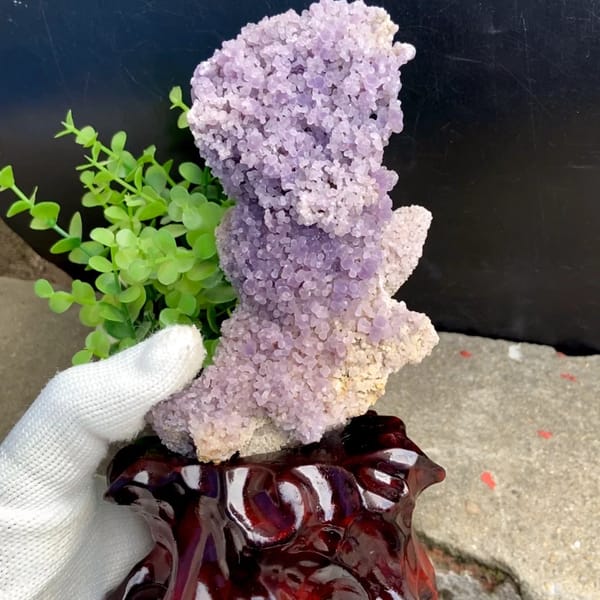 Tower of purple grape agate on carved stand from Indonesia, held in gloved hand