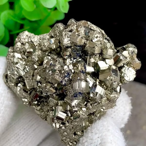 Rounded cluster of bright pyrite dodecahedra from Peru, held in gloved hand