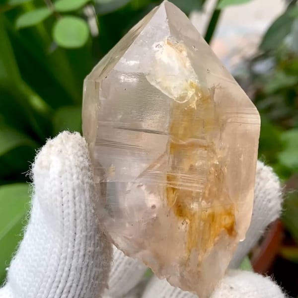 Transparent single quartz crystal with golden phantom from Sichuan, China, held in gloved hand