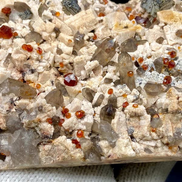 Bar of feldspar dotted with Fanta-orange spessartine and smoky quartz from Yunxiao, Fujian, close-up of the crystal faces