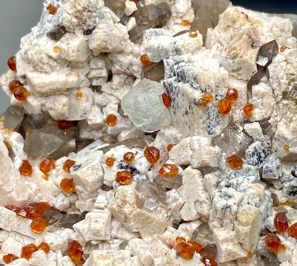 Bar of feldspar dotted with Fanta-orange spessartine and smoky quartz from Yunxiao, Fujian, detail of the matrix contact