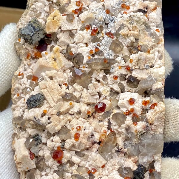 Bar of feldspar dotted with Fanta-orange spessartine and smoky quartz from Yunxiao, Fujian, China, side view