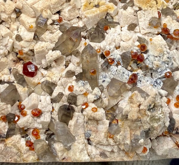 Bar of feldspar dotted with Fanta-orange spessartine and smoky quartz from Yunxiao, Fujian, China, close-up of terminations