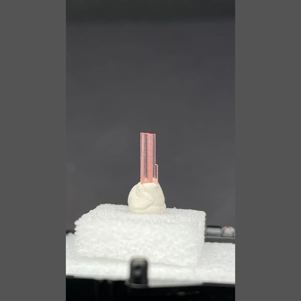 Tiny pale pink väyrynenite crystal on a display stand from Pakistan — alternate view