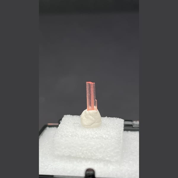 Tiny pale pink väyrynenite crystal on a display stand from Pakistan — detail view