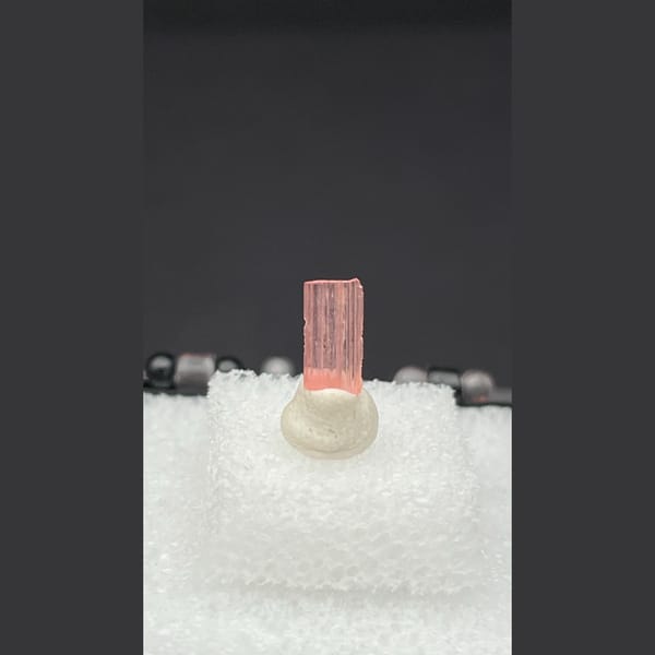 Tiny pale pink väyrynenite crystal on a display stand from Pakistan — alternate view