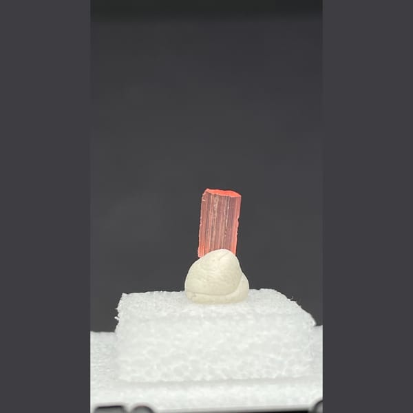 Tiny pale pink väyrynenite crystal on a display stand from Pakistan — alternate view