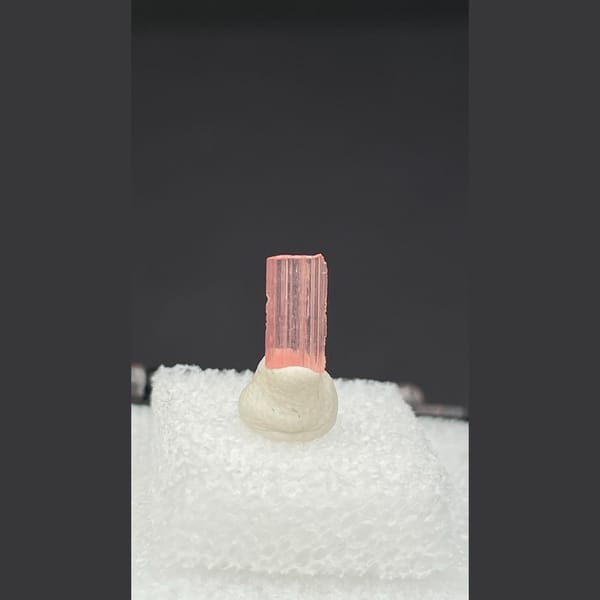 Tiny pale pink väyrynenite crystal on a display stand from Pakistan — detail view