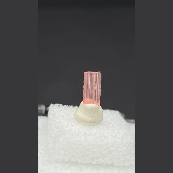 Tiny pale pink väyrynenite crystal on a display stand from Pakistan — detail view