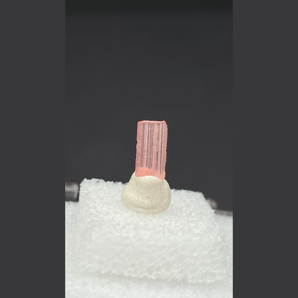 Tiny pale pink väyrynenite crystal on a display stand from Pakistan — detail view
