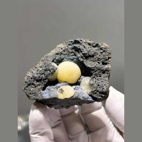 Round butter-yellow calcite spheres in dark rock pocket from Zhejiang — complete view