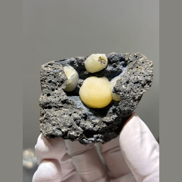 Round butter-yellow calcite spheres in dark rock pocket from Zhejiang — alternate view