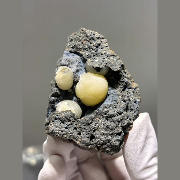 Round butter-yellow calcite spheres in dark rock pocket from Zhejiang — alternate view