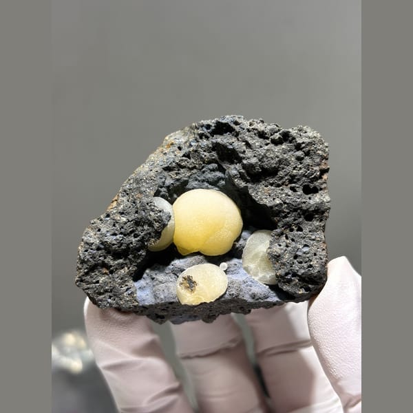 Round butter-yellow calcite spheres in dark rock pocket from Zhejiang — detail view