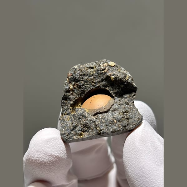 Peach calcite sphere in a dark matrix pocket from Zhejiang — complete view