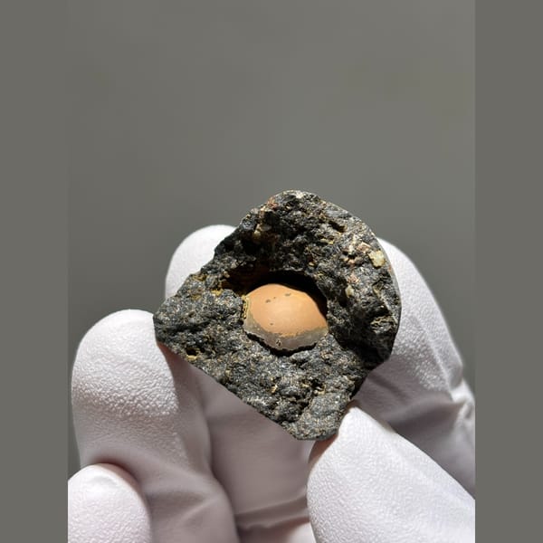 Peach calcite sphere in a dark matrix pocket from Zhejiang — alternate view