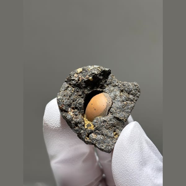 Peach calcite sphere in a dark matrix pocket from Zhejiang — alternate view