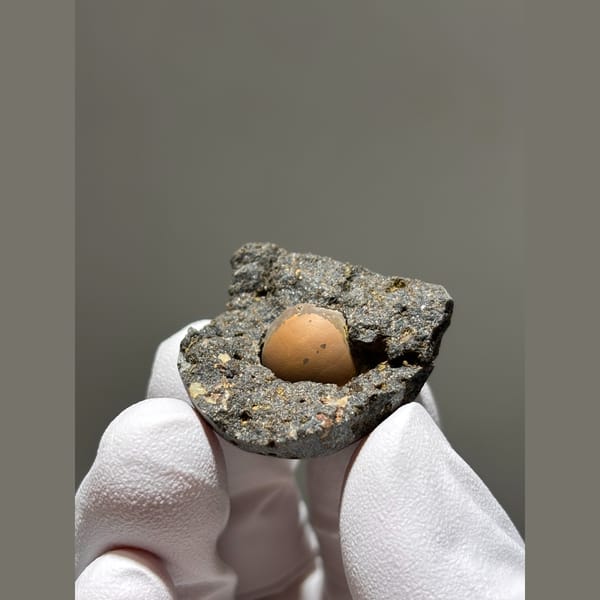 Peach calcite sphere in a dark matrix pocket from Zhejiang — detail view