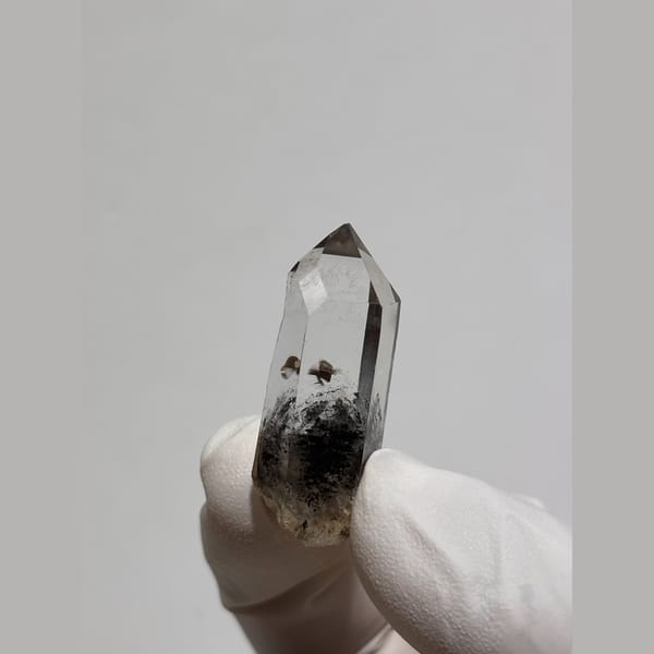 Slender clear quartz point with dark inclusions from Jinkouhe — complete view