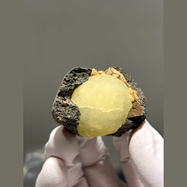 Pale yellow calcite ball in dark matrix pocket from Zhejiang — alternate view