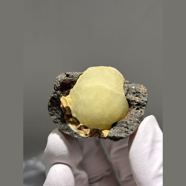 Pale yellow calcite ball in dark matrix pocket from Zhejiang — detail view