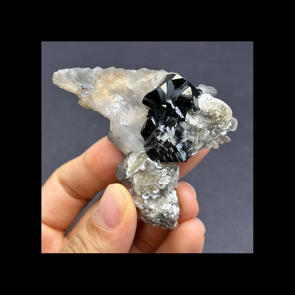 Complete front view of black cassiterite, fin-shaped calcite and silvery mica from Xuebaoding
