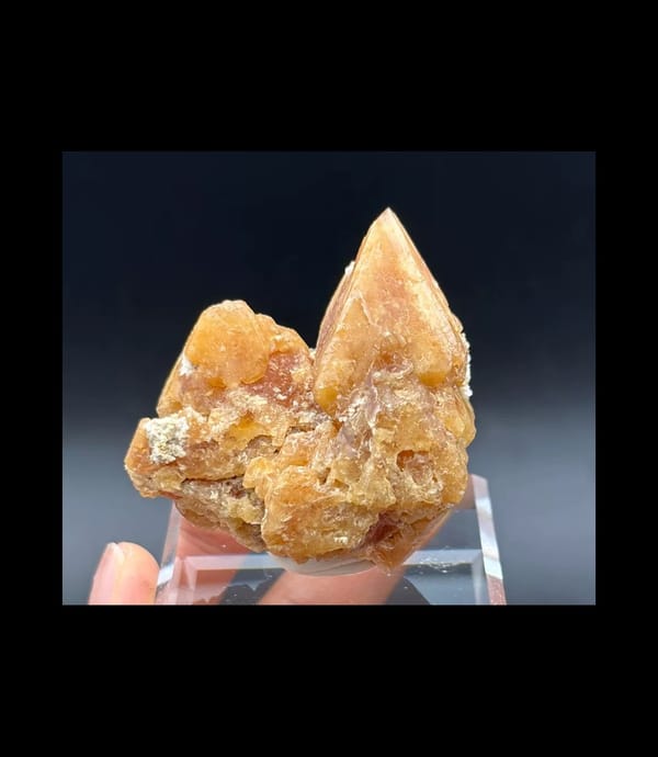 Complete front of amber-orange scheelite showing one tall pointed peak and lower neighbouring crystals