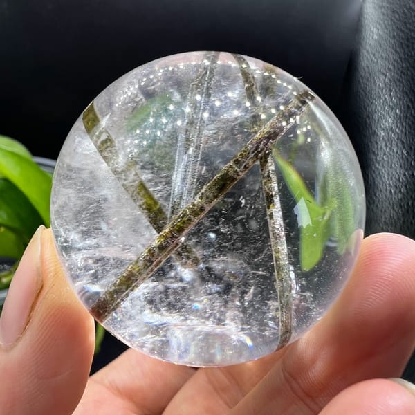 Clear quartz sphere with green tourmaline inclusions — detail view