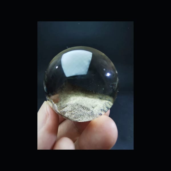 Complete front view of the exact slightly smoky ghost quartz sphere and its low dune-like inclusion