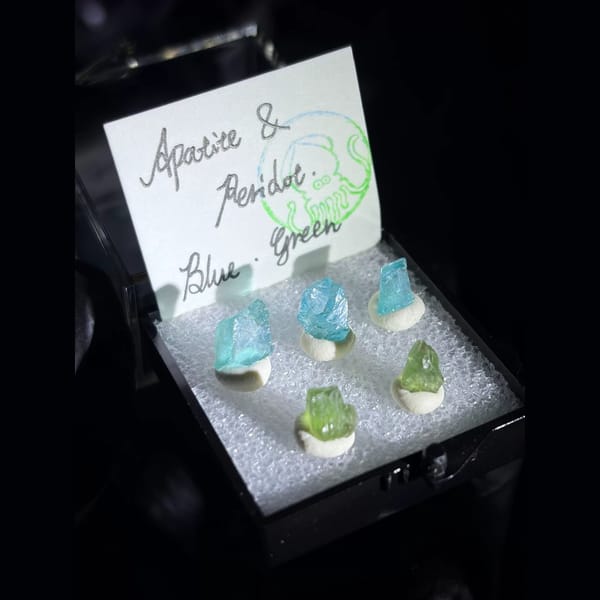 Blue apatite and green peridot crystals in a small display box — alternate view