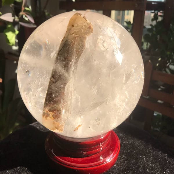 Clear quartz sphere with a thick golden included rod from Brazil — alternate view