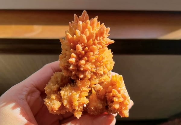 Complete handheld front view of the exact orange crystallized mineral specimen
