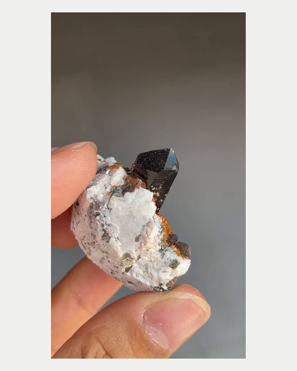 Complete left oblique view of smoky quartz with spessartine and feldspar