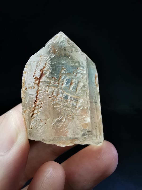 Complete angled view showing the transparent quartz point and red-toned surface traces