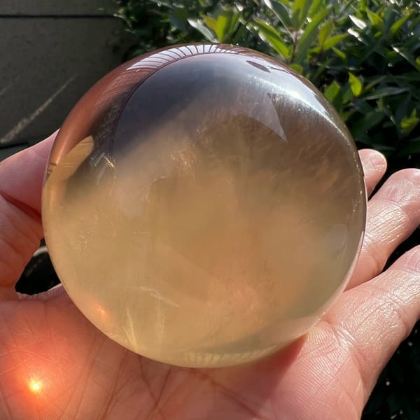 Citrine sphere backlit in hand, smoky reflection across the top and white wisps