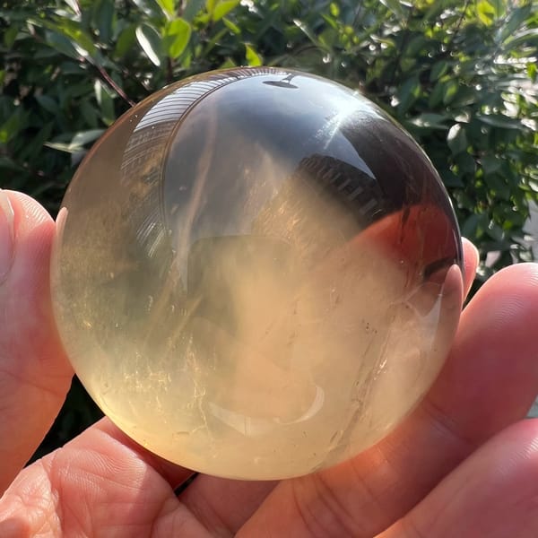 Sunlit citrine sphere with feathery white inclusions rising from the bottom