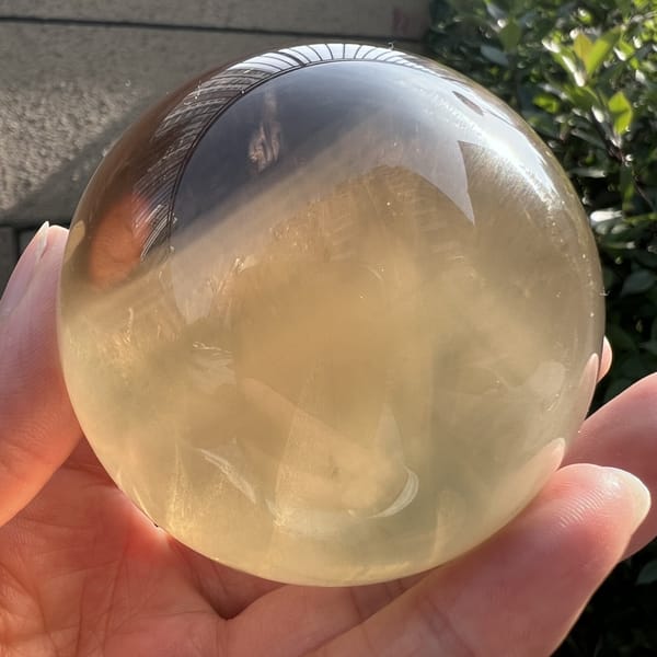 Golden citrine sphere held outdoors, misty white inclusions through the middle