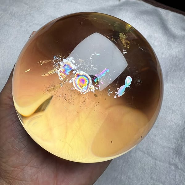 Golden citrine sphere on pale cloth with a cluster of rainbow rings near the centre