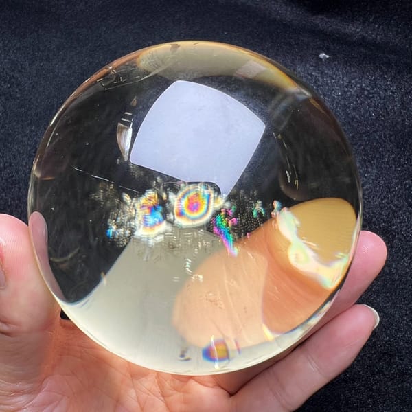 Clear citrine sphere in hand showing vivid rainbow inclusions and window reflection