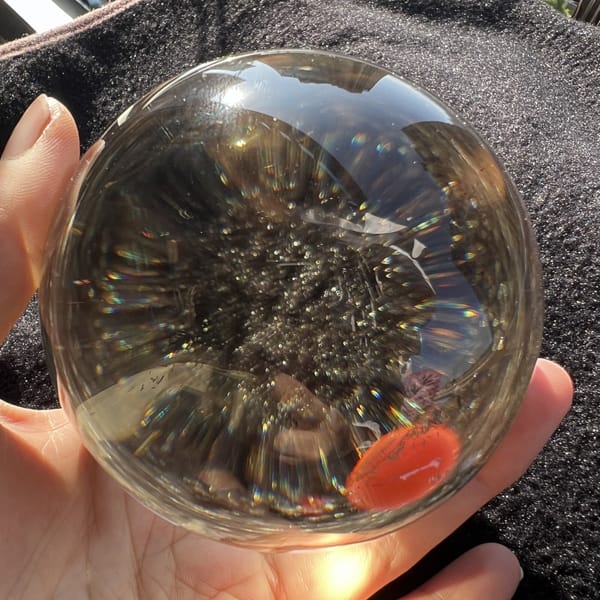 Rutile cloud and soft rainbows inside the citrine sphere on dark foam
