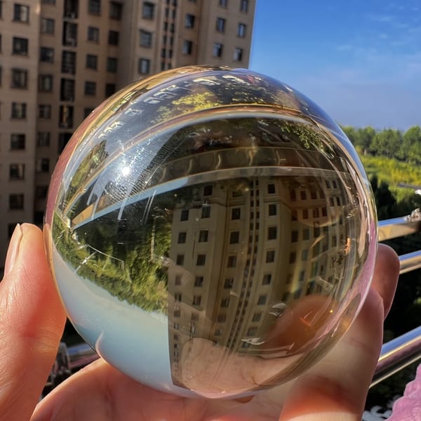 Clear citrine sphere held against blue sky with building reflection