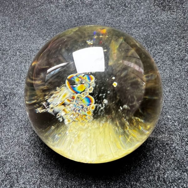 Golden citrine sphere with stacked rainbow inclusions and a bright highlight
