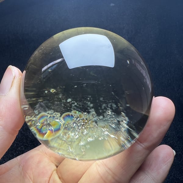 Citrine sphere with rainbow rings at the lower left on a dark backdrop